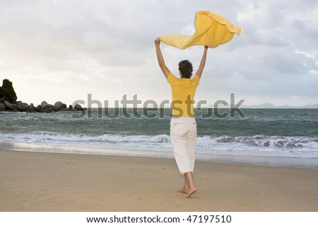 Happy woman walking on a beach with a towel in the wind
