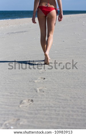 A girl with a red bikini walks alone alone a beach