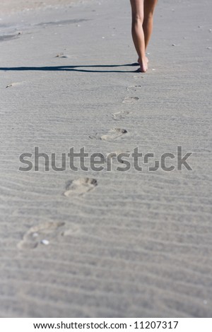 Woman walking away from the camera on a beach leaving footprints