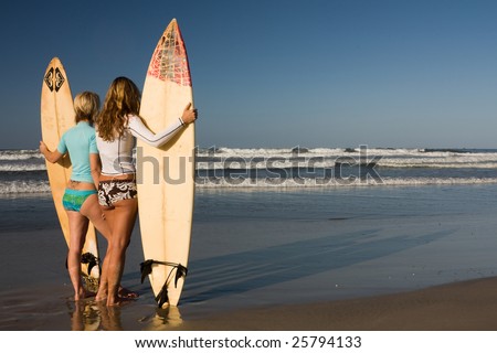 stock photo : Two girls standing with surfboards at dawn looking out to the 