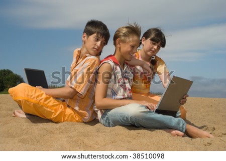 Three teens  with laptops on sea sand