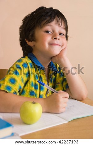 The boy with write-book and green apple and pencil in the classroom