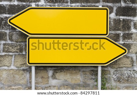 direction signs with wall in background. yellow signs. arrow shape