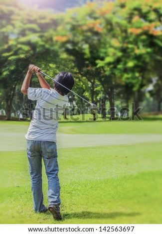 Male golf player teeing-off golf ball at beautiful golf course with forest.