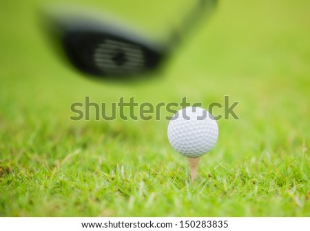 Golf ball behind driver at driving range, plenty of copy-space and very shallow depth of field.
