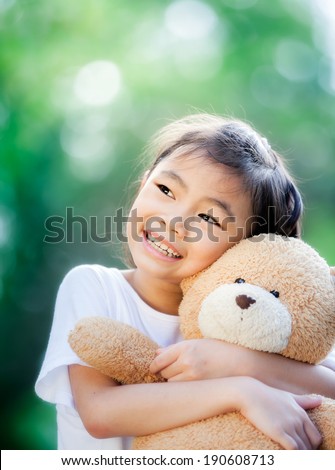 Little Asian girl with teddy bear in park.