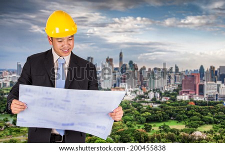 Asian civil engineer in hardhats taking a look at the blueprint in urban environment
