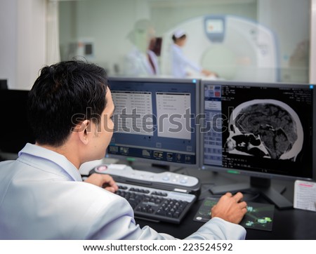 Medical team operating computers in CT scan lab for head section