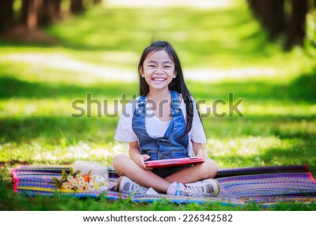 Funny little Asian girl learning with tablet pc in the park
