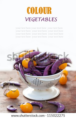 Fresh purple beans and yellow tomatoes in the white colander with space for text.