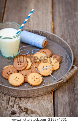 Sugar cookies in shape of buttons on wooden table with a glass of milk.  Also available in horizontal format.