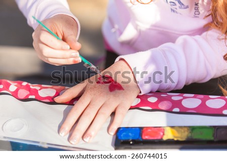 Little girl paining hearts on her hand.