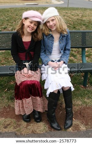 young girl friends smiling and sitting on bench at park