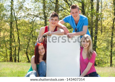 Four teenagers in colored shirts and a white board which can be used for your advertisements