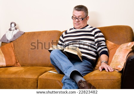 Older man reading a book sitting on his couch