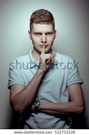 Portrait of young handsome guy with silence finger gesture.