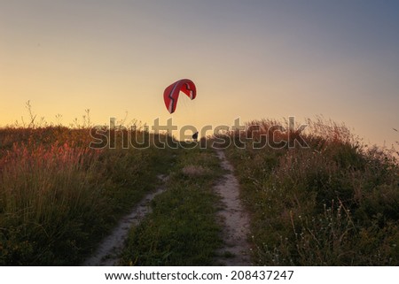 Rural road at sunset. Paraglider canopy over it.