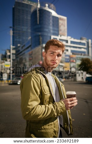 City style. Handsome young man in smart casual wear holding coffee cup and looking away while standing at the street.