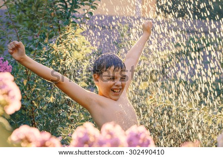 Summer fun. Excited 11-years boy enjoying water shower in the garden. Water drops in sunlight.