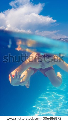 Boy swimming and diving in blue pool with fun - split shot underwater and summer sky above.