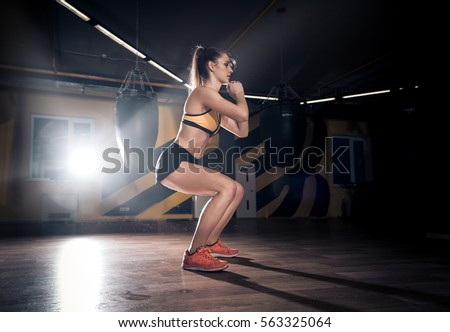 Sportive young woman making squats in a gym training. Working out in a fitness gym.