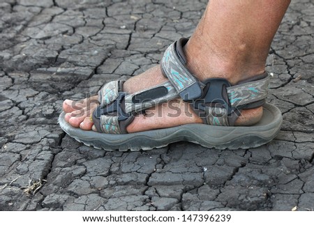 dirty human foot in sandals on the cracked earth