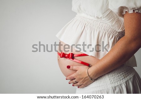 Beautiful belly of young attractive pregnant woman tied with a red bow