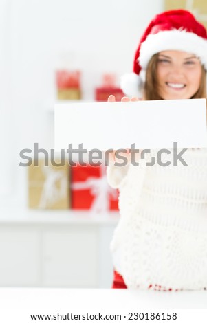 Santa girl peeking from behind blank sign billboard. Advertising photo of young smiling Christmas woman in Santa hat showing paper sign.
