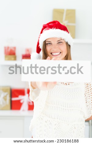 Santa girl peeking from behind blank sign billboard. Advertising photo of young smiling Christmas woman in Santa hat showing paper sign.