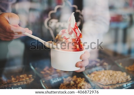 seller pours sauce on a soft frozen yoghurt in white take away cup in cafe