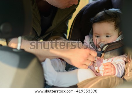 A father putting his baby daughter into her car seat in the car