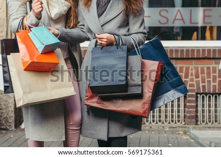 two girls with shopping bags in front of show-window with sale written on it, close up