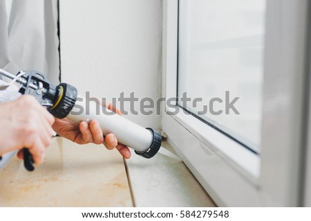 Hands of worker using a silicone tube for repairing of window indoor