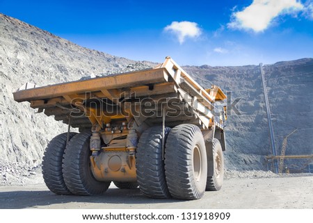 Heavy mining dump truck driving along the opencast. Ore conveyor at background