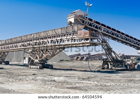 a large conveyor belt carrying golden ore and emptying onto a huge pile