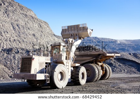 Wheel front-end loader unloading  ore into heavy dump truck at the opencast mining