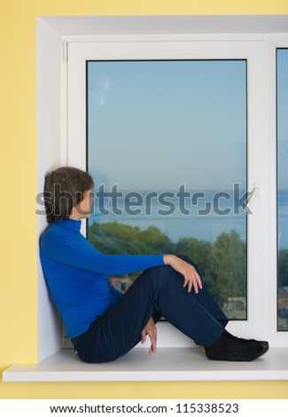 the woman looks at a landscape behind a window