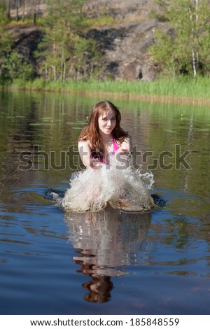 teenage girl plays with water in summer lake