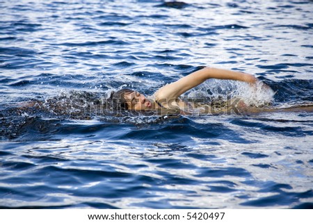 woman swimming the crawl through the blue forest lake