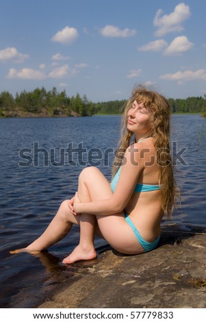 The girl sunbathes in hot day on the bank of lake