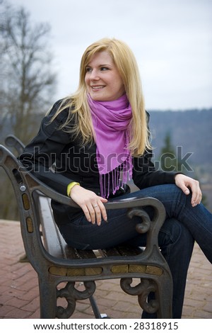 Young blond beautiful girl sitting on the bench and looking left