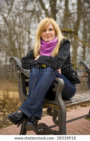 Young blond beautiful girl sitting on the bench in a funny posture and smilling
