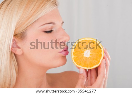 Beautiful young blond female on a diet kissing juicy orange