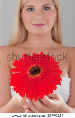 Young atractive woman with pure makeup in a background holding a red flower