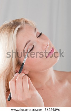 Picture of a young healthy naturally looking girl applying a make up with a brush