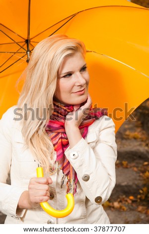 Picture of a young happy woman standing under yellow umbrella in an autumn park