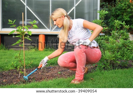 Young smiling attractive blond girl working in the garden near the greenhouse