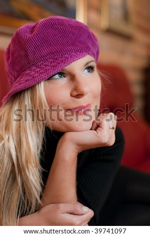 Young beautiful romantic dreaming woman on red sofa in a hat