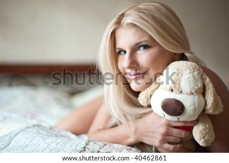 young beautiful woman with pure healthy skin holding a little toy in her bed