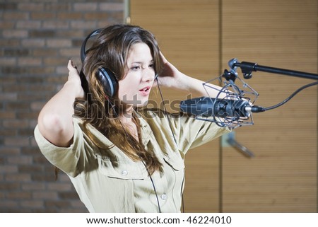 Young beautiful retro woman recording the sound in professional studio with mic and phones. indoor